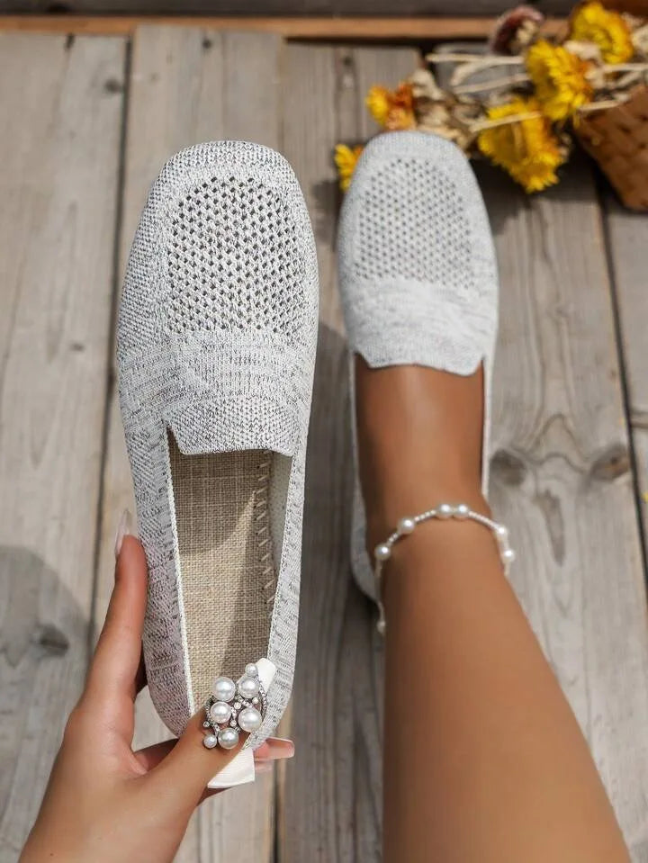 Pale grey knit loafers with woven texture, displayed outdoors on wood decking beside dried flowers