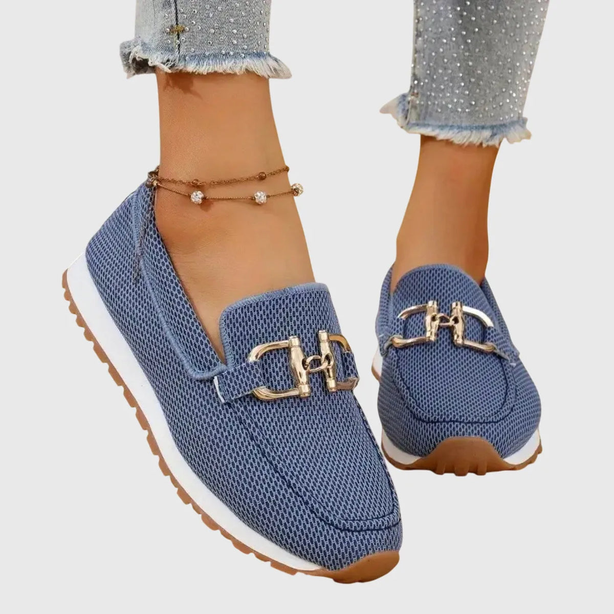 Close-up front view of a white knit slip-on loafer with gold horsebit trim on a model's foot