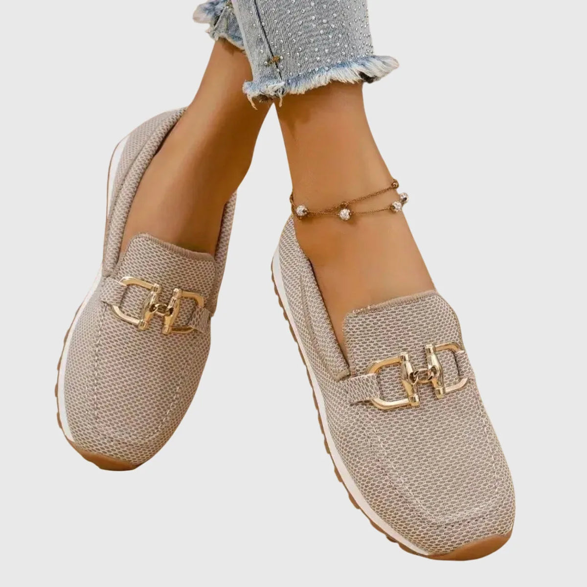 Model walking on a gravel garden path wearing beige knit slip-on loafers with gold trim