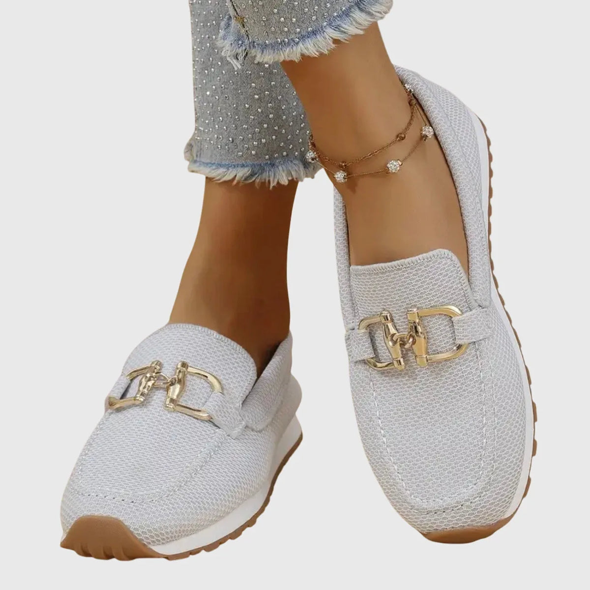 Close-up of beige knit loafers on crossed feet, highlighting the gold buckle and tan outsole