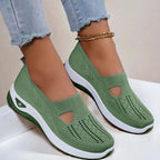 Side view of army green knit slip-on shoes with cut-out detail and white platform sole, worn with cuffed denim jeans