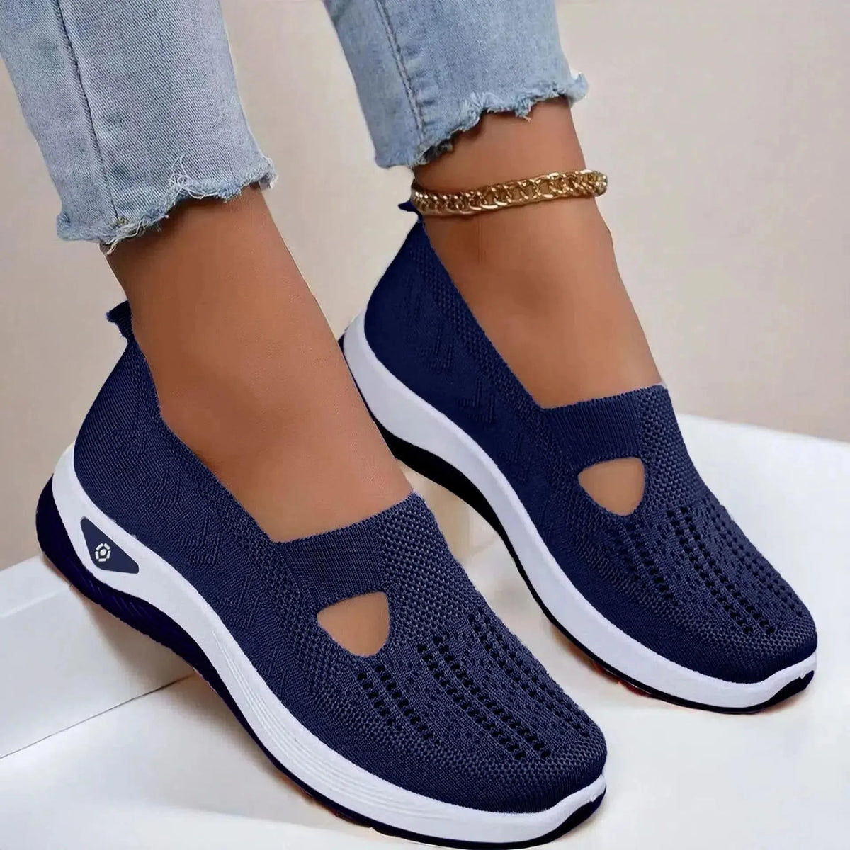 Side view of navy blue knit slip-on shoes with cut-out detail and white platform sole, styled with light denim jeans