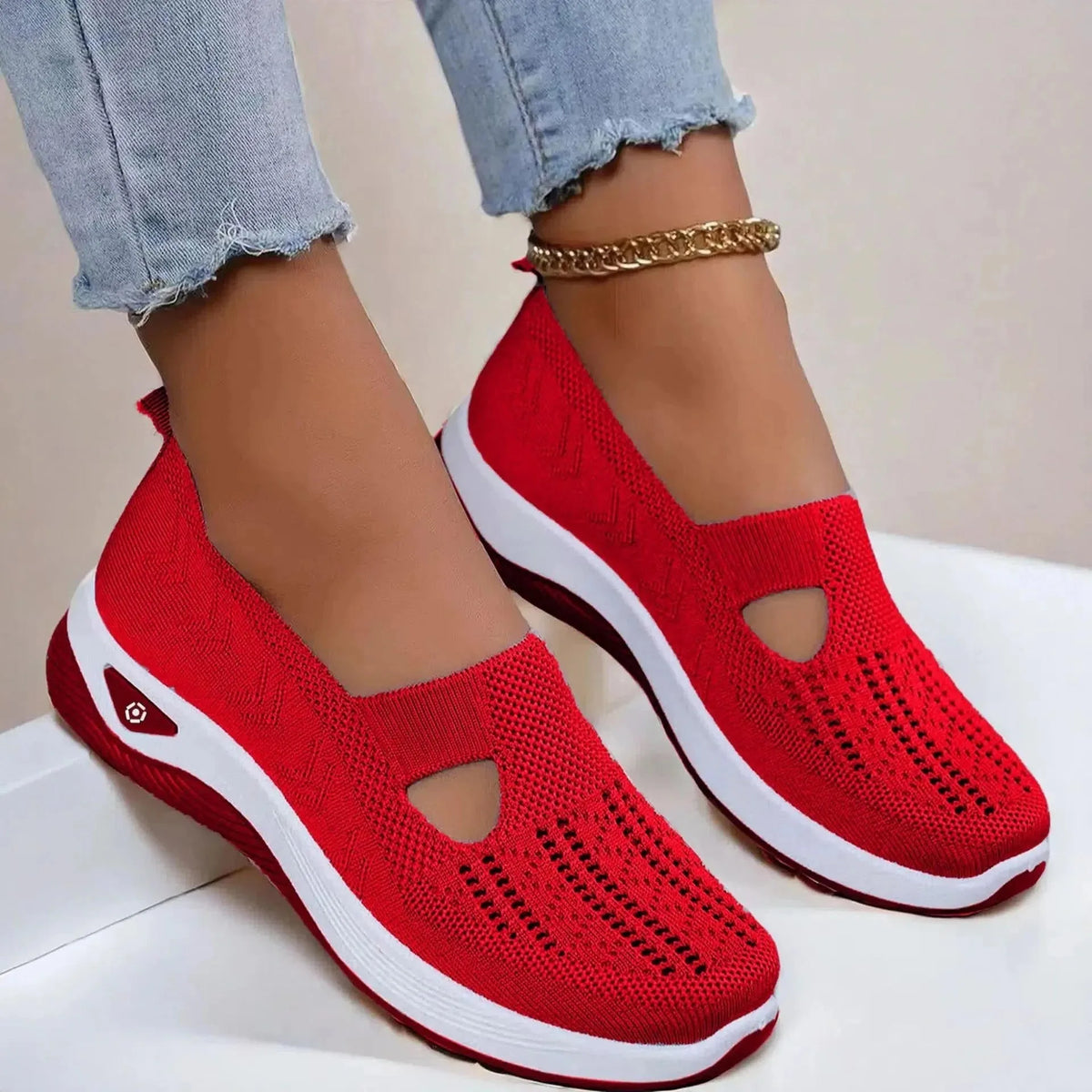 Side view of red knit slip-on shoes with cut-out vamp detail and white platform sole, worn with rolled denim jeans