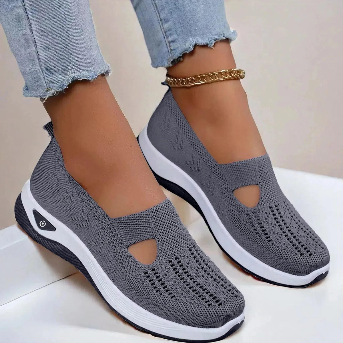 Side view of dark grey knit slip-on shoes with cut-out detail and white platform sole, styled with light denim jeans