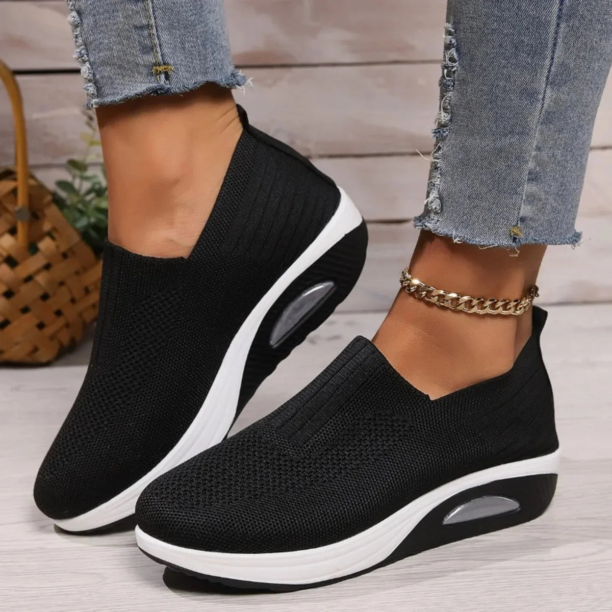 Side view of black knit slip-on sneaker worn on foot, showing V-cut collar and chunky white midsole