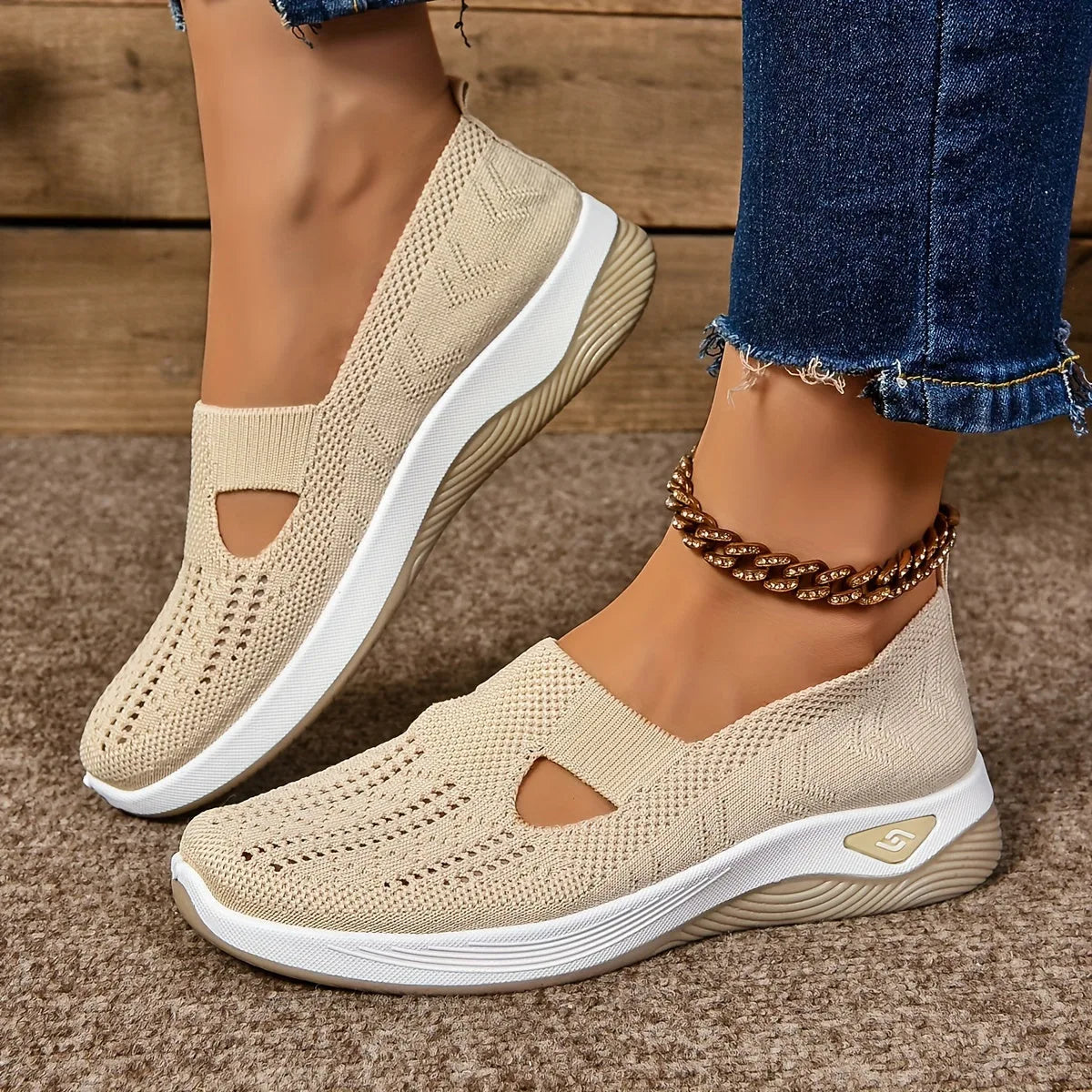 Side angle of cream mesh knit slip-on sneaker showing teardrop cut-out and tan ribbed outsole, paired with denim and a gold anklet