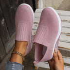 Close-up of pink knit slip-on sneakers held by hand, showing ribbed heel panel and white platform sole