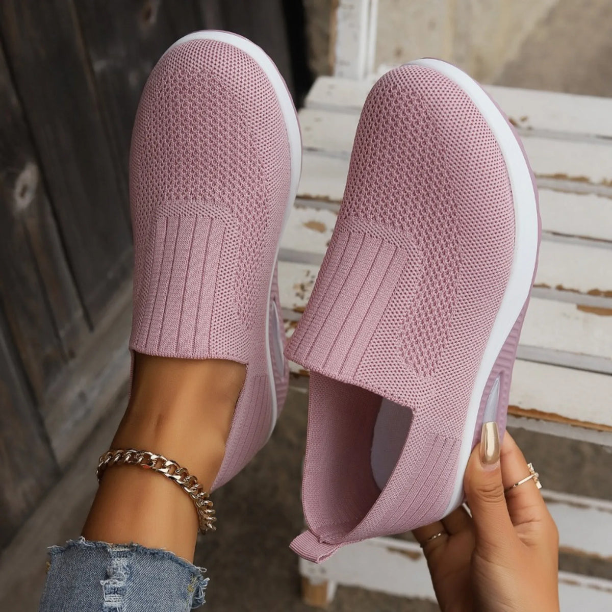 Close-up of pink knit slip-on sneakers held by hand, showing ribbed heel panel and white platform sole