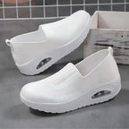 Pair of white knit slip-on sneakers displayed on concrete, showing air-cushion heel detail and textured sole