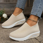 Beige knit slip-on sneakers worn on feet, showing soft ribbed collar and white thick sole