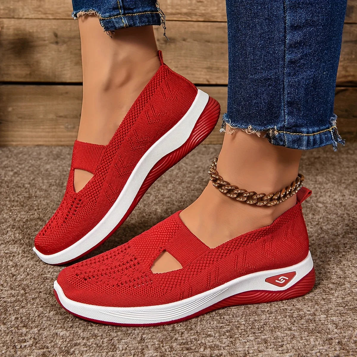 Side profile of red knit slip-on shoes with cut-out detail and matching red sole, styled with rolled denim and a gold anklet