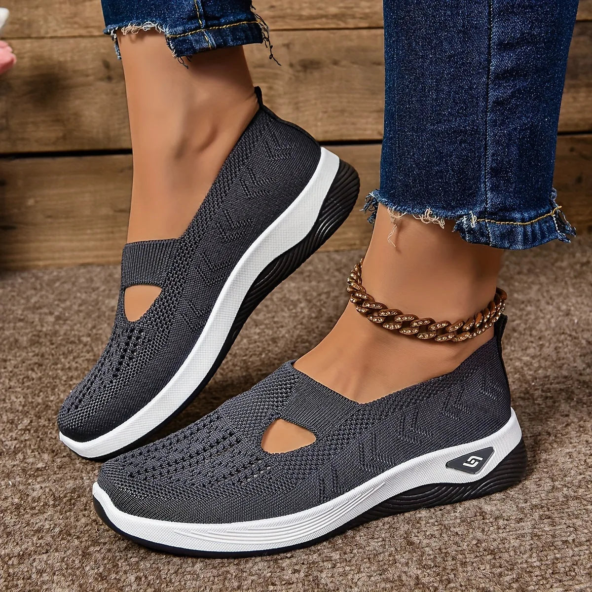 Side view of charcoal grey knit slip-on sneakers with teardrop cut-out and white ribbed outsole on a textured rug background