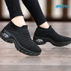 Side view of a black knit sock-style sneaker with air cushion sole, worn while walking in black leggings