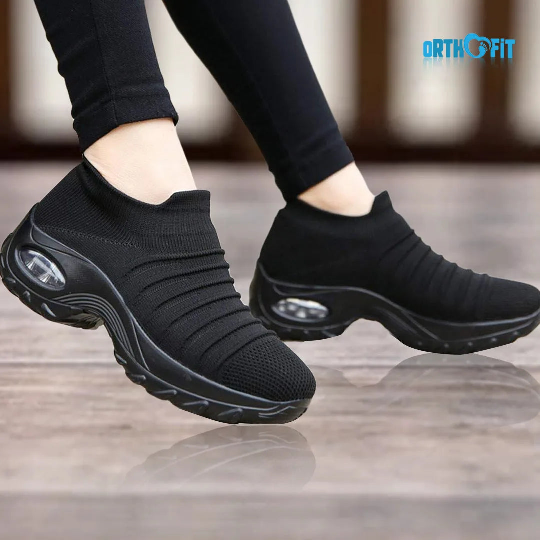 Side view of a black knit sock-style sneaker with air cushion sole, worn while walking in black leggings