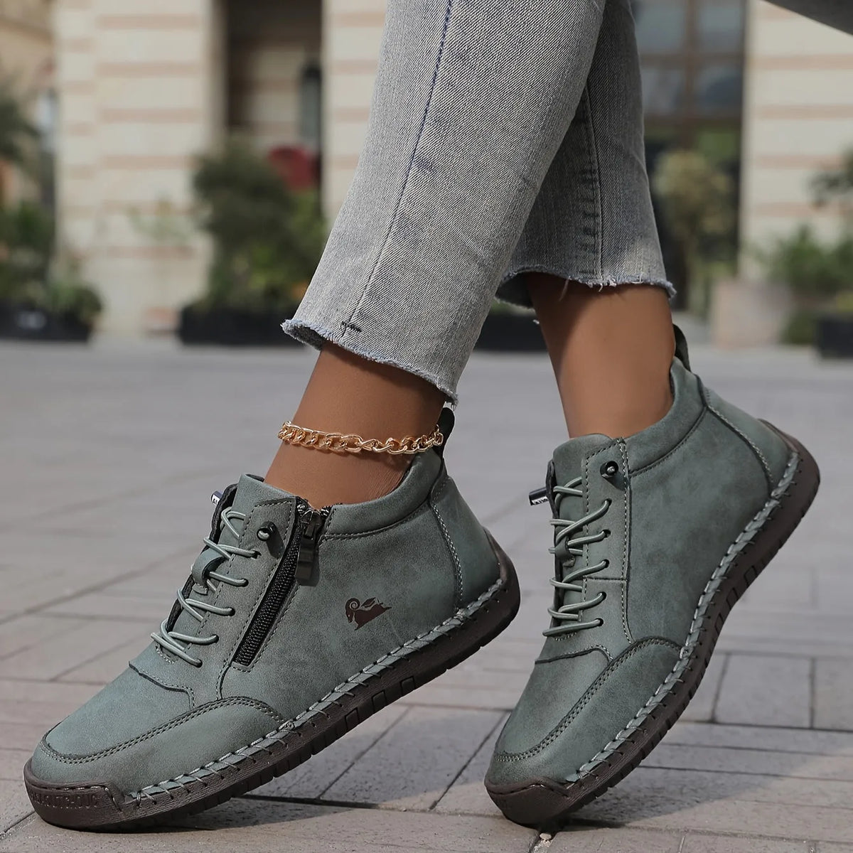 Side view of sage green lace-up ankle boots with side zip, worn by a model stepping forward on a stone pavement