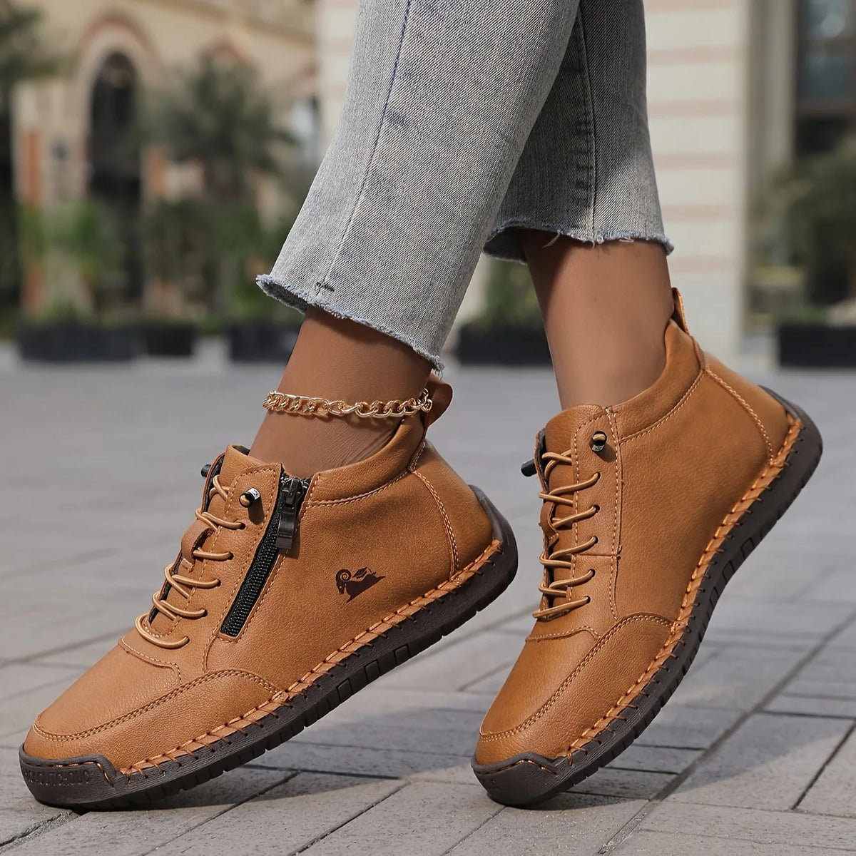Tan brown lace-up ankle boots with visible hand-stitched leather trim, worn while walking on a cobbled street