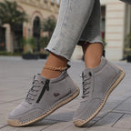 Grey suede-look ankle boots with tan sole and side zip, shown mid-stride on a tiled footpath