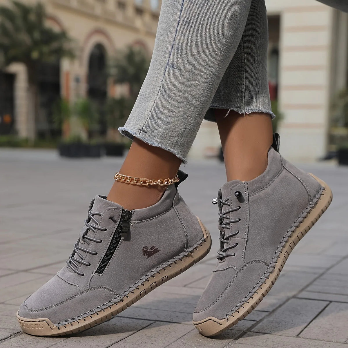 Grey suede-look ankle boots with tan sole and side zip, shown mid-stride on a tiled footpath