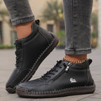 Black leather ankle boots with contrast stitching and silver zip, photographed from the side while walking