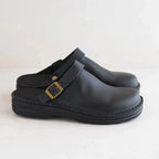 Side view of black leather clog with brass-tone buckle strap and matching black sole