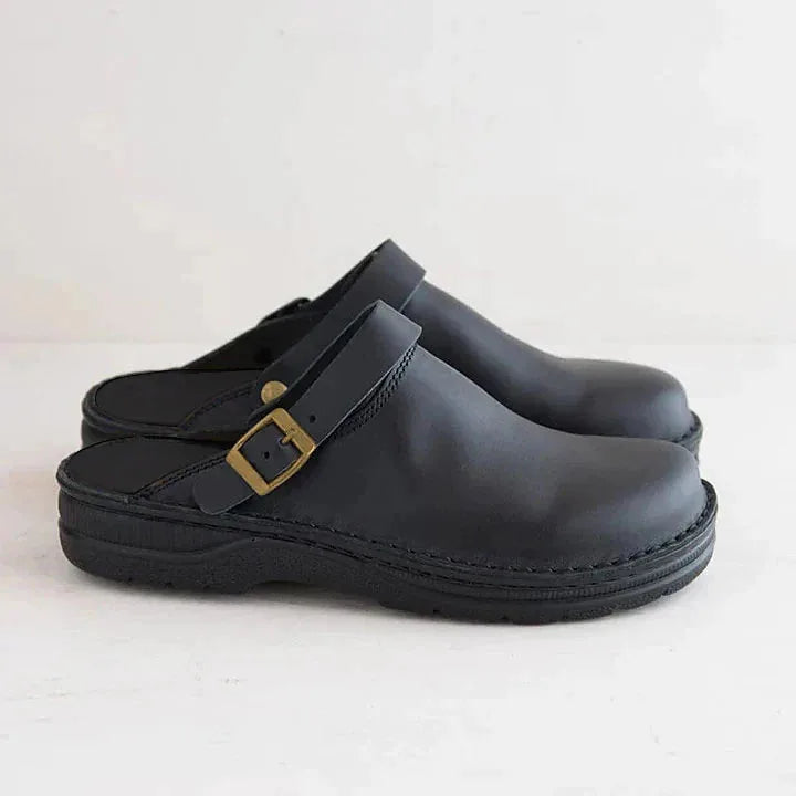 Side view of black leather clog with brass-tone buckle strap and matching black sole
