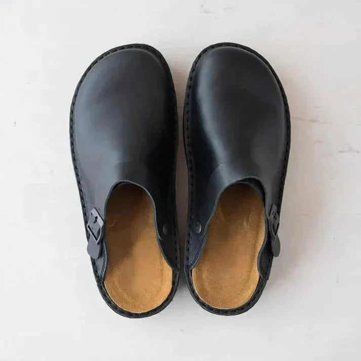 Top-down view of a pair of black leather clogs showing tan leather footbed and rounded toe