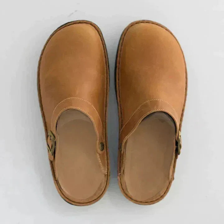 Top-down view of a pair of tan leather clogs showing stitched trim and buckle strap detail