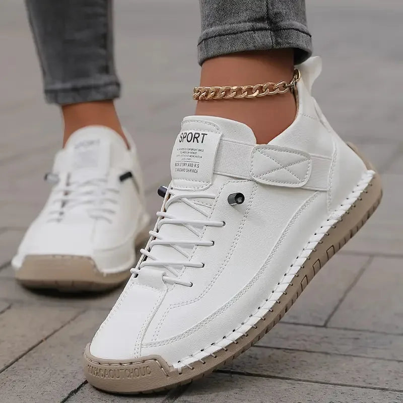 White leather sneaker with lace-up front, visible hand-stitched trim, and gold anklet chain worn on foot