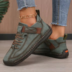 Pair of olive green sneakers with tan stitching detail and orange heel accent, shown on wooden floor