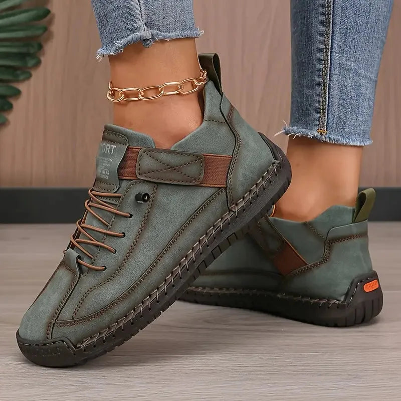 Pair of olive green sneakers with tan stitching detail and orange heel accent, shown on wooden floor