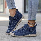 Navy blue suede sneaker with tan sole and hand-stitched panels, worn with cuffed denim jeans