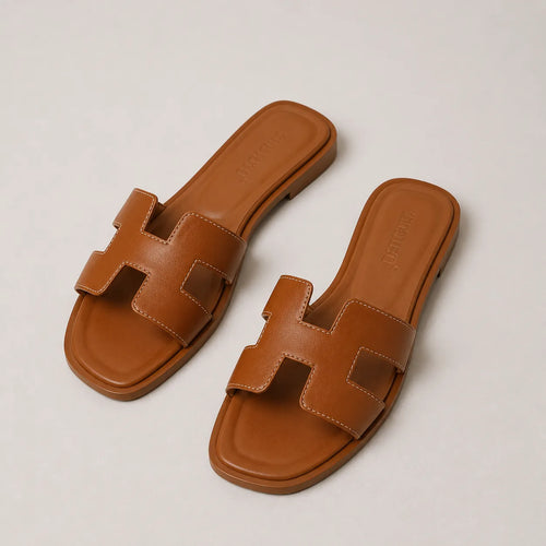 Flat-lay of a pair of tan leather slide sandals with H-strap design, square toe and stitched detailing