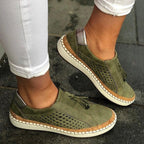 Side view of olive green perforated suede slip-on sneaker with cork-trim sole and tassel detail, worn with white jeans