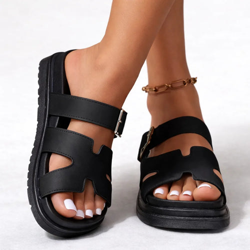 Side view of black platform sandal with cut-out strap design and silver ankle buckle, worn barefoot with gold anklet