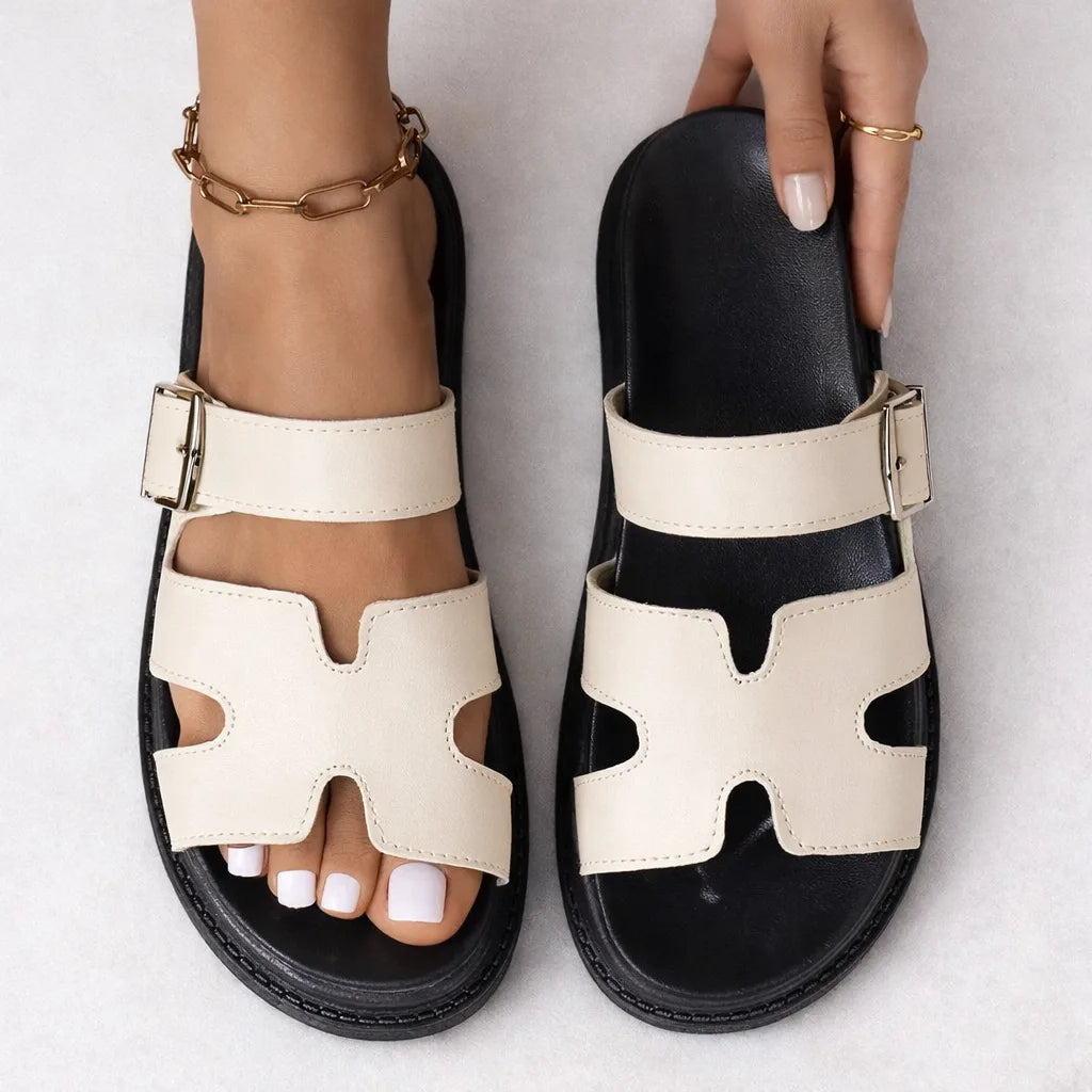Top-down view of cream platform sandals with ankle strap and buckle, one held by hand to show footbed and sole