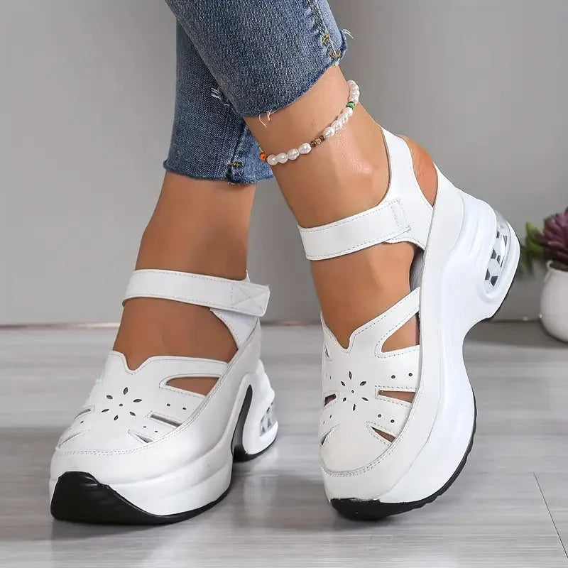 Side view of white chunky platform sandal with ankle strap, cut-out floral detail, and air-cushion wedge sole