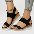 Side view of black woven wedge sandal with ankle strap, espadrille platform and gold anklet accent