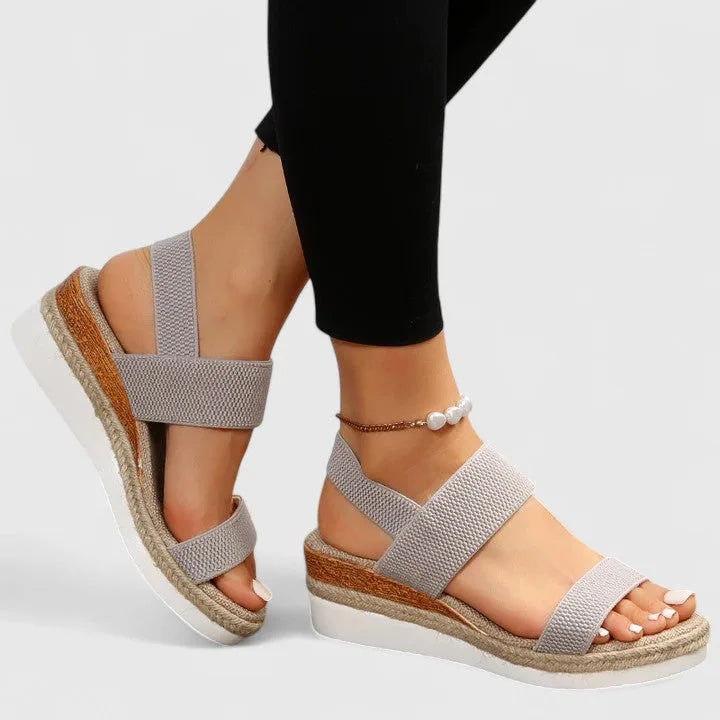 Side profile of pink wedge sandal with elastic straps and woven jute wedge against black leggings