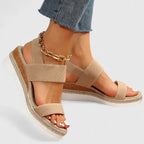 Close-up of beige wedge sandal with crisscross elastic straps and gold anklet, worn with cropped denim