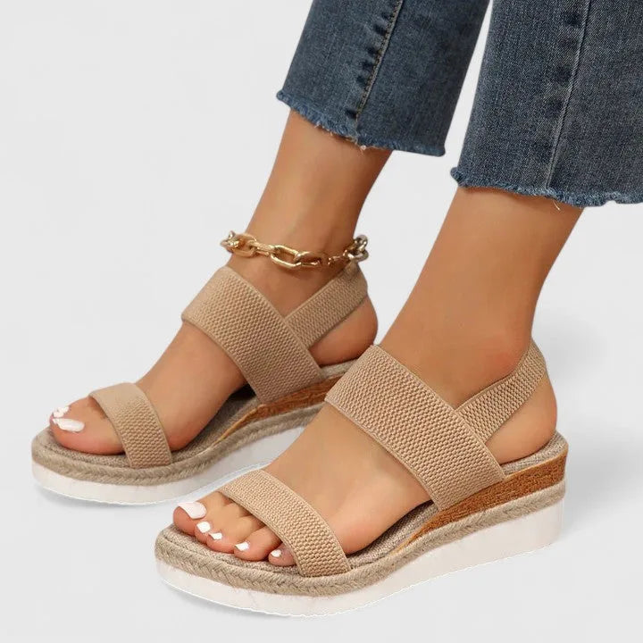 Pair of beige wedge sandals with elastic straps and white platform sole, styled with denim jeans