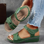Green wedge sandal with perforated strap cutouts and padded insole, held beside a model's ankle for size reference