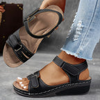 Black wedge sandal with contrast stitching and dual adjustable straps, showing the ankle fit from the side