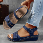 Navy blue wedge sandal with perforated detailing and secure ankle closure, shown worn with cuffed denim