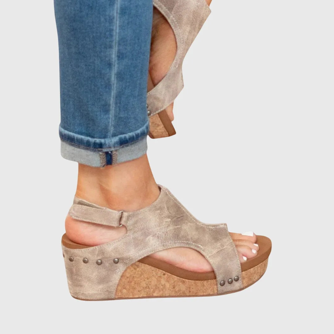 Side profile of beige wedge sandal highlighting cork platform height, cut-out sides and stitched leather panel