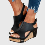 Front view of black wedge sandals with peep toe, shield vamp and cork platform sole worn with cuffed jeans