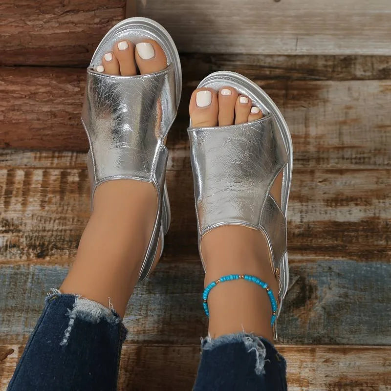 Overhead view of feet in silver metallic wedge sandals with open toe and crossover strap