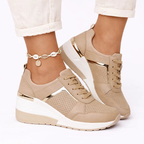 Side view of beige wedge sneaker with gold-tone trim and perforated panel, worn with an ankle shell bracelet