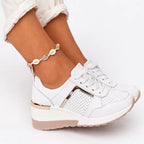 White lace-up wedge sneaker with mirrored gold side panel and perforated toe detail, shown on foot