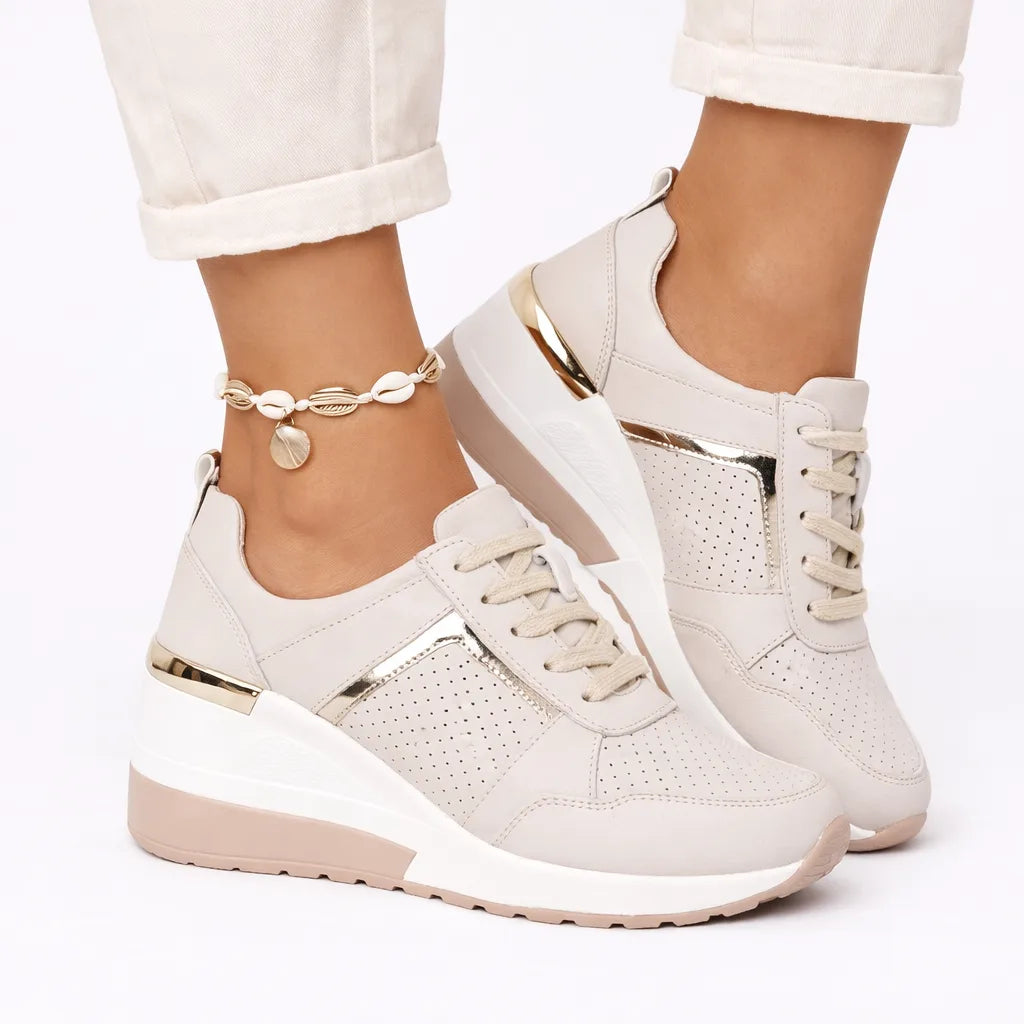 Close-up front angle of beige wedge sneaker showing gold trim, perforated leather and lace-up fastening
