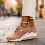 Tan wedge sneakers with metallic gold heel strip and perforated toe, worn with cream cuffed trousers and anklet